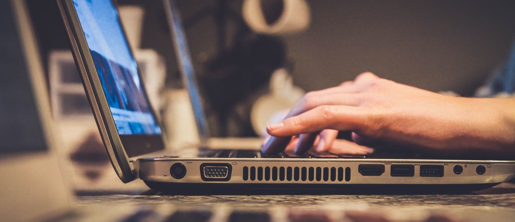 Phishing emails - side view of an open laptop on a desk with a hand typing on the keys.