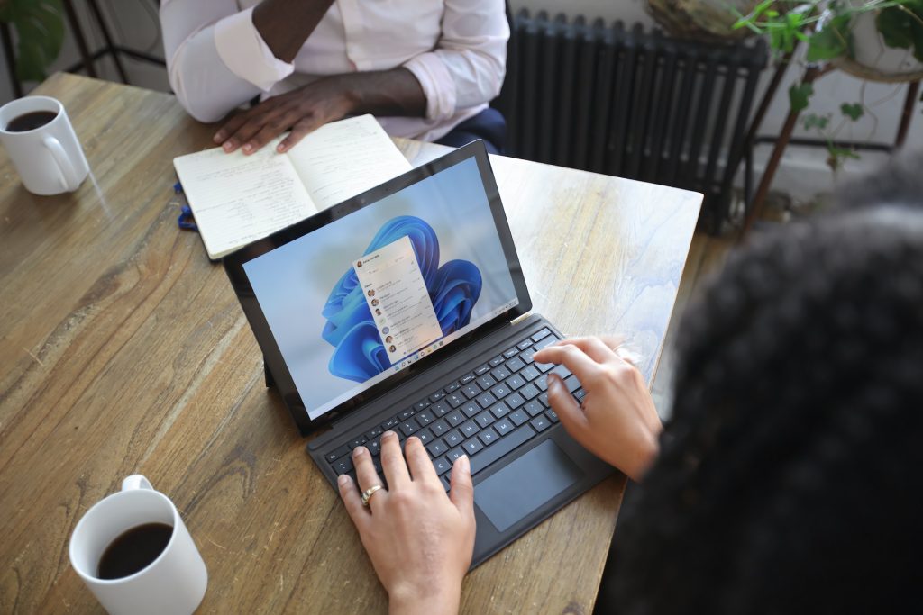 Microsoft Forms - two people sitting opposite each other at a meeting room table with a Windows laptop between them and two cups of coffee