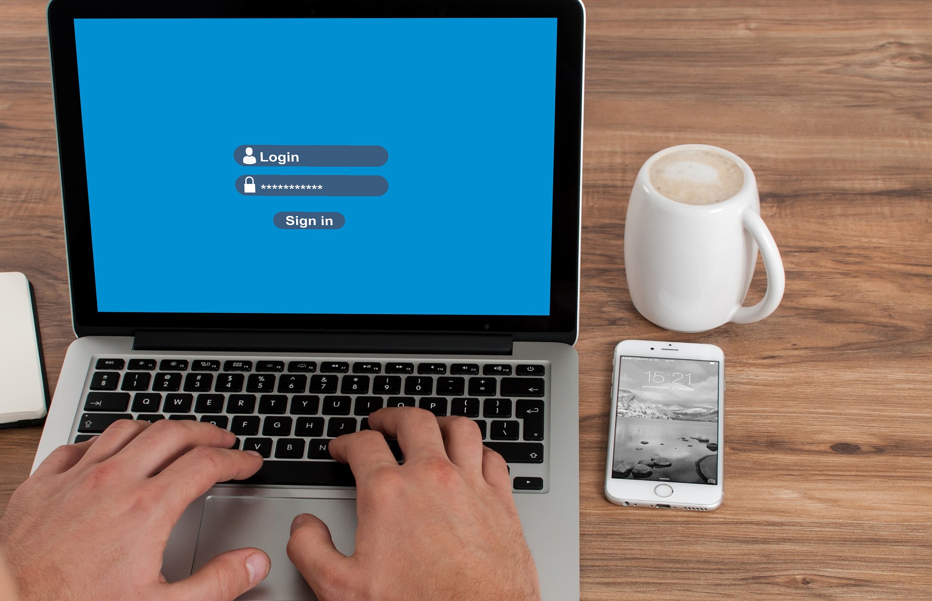 Secure Passkeys - image of a latop on a desk with a coffee cup and phone on the desk to the right of the machine. Laptop is open on the login screen.